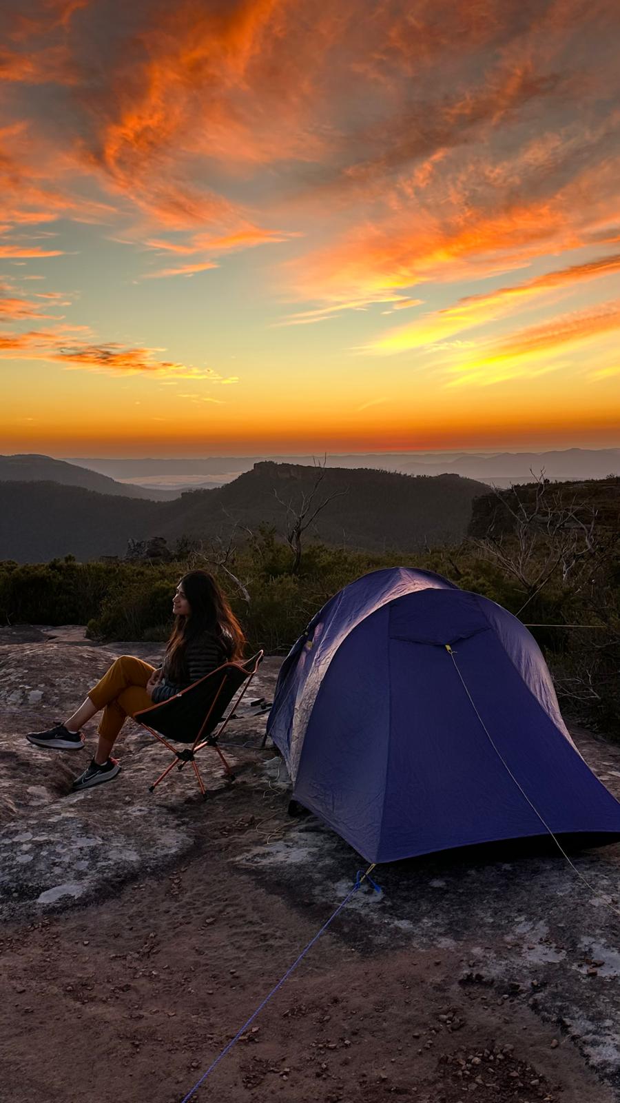 Amna sitting beside a tent at sunset, looking out over the mountains