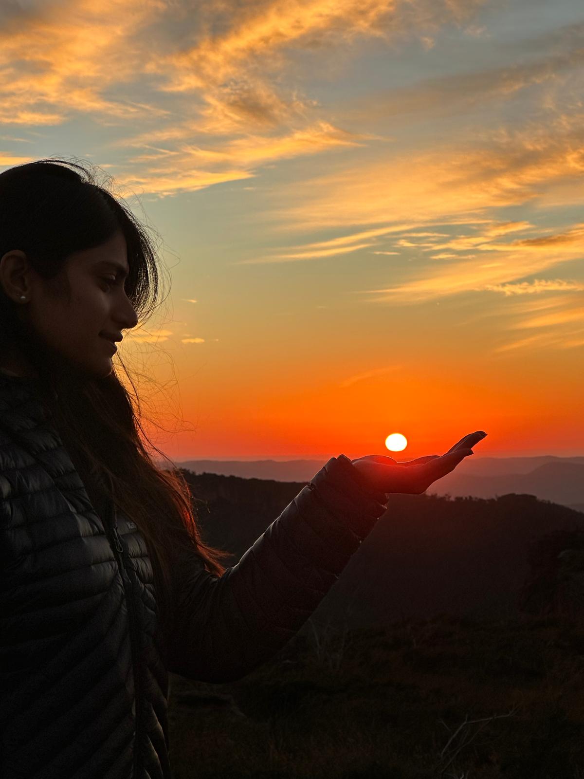 Amna silhouetted against a golden sunrise over the mountains